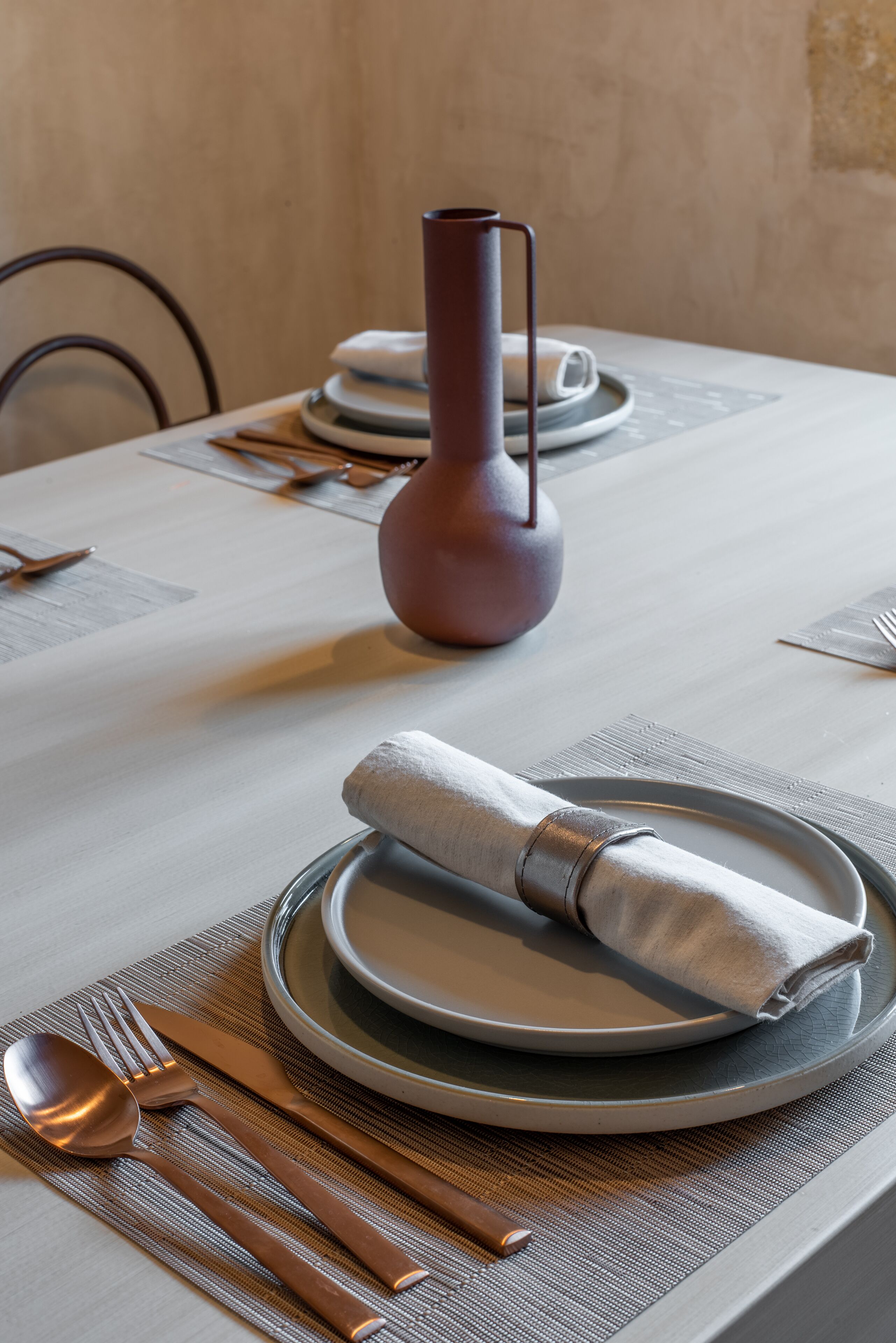 A neatly set dining table with plates, cutlery, and a vase.