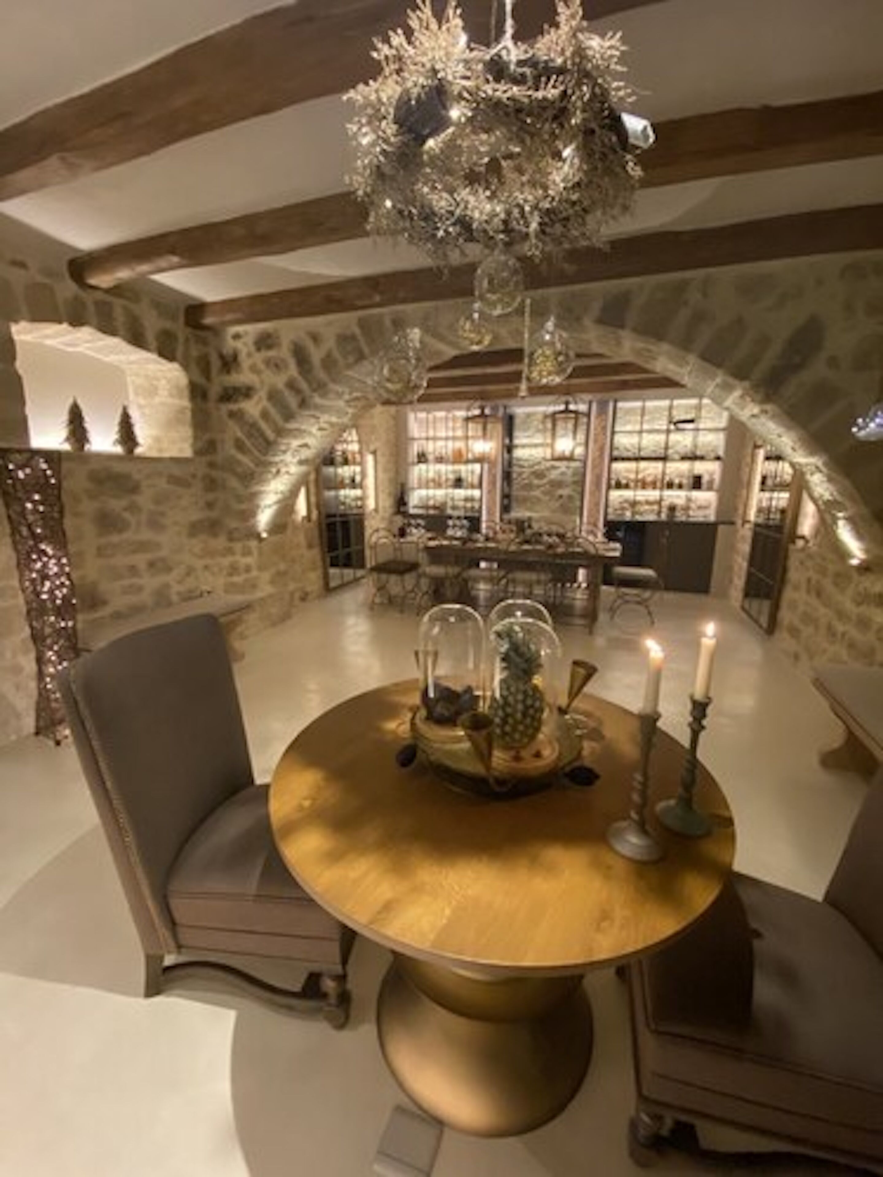 Un espace repas avec une table ronde, des chaises, un lustre et un mur en pierre en arrière-plan.
