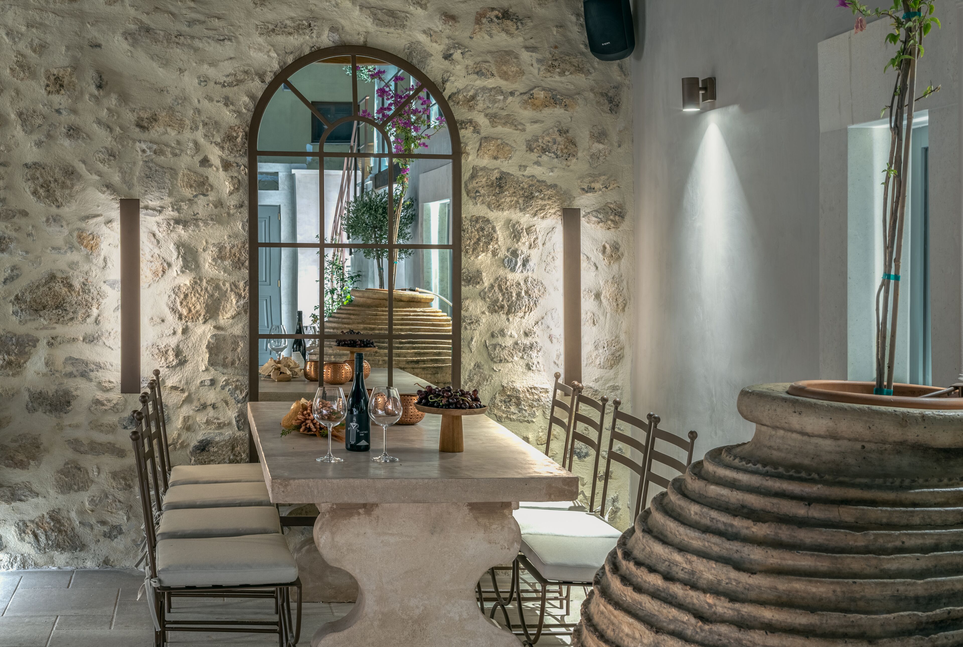 Comedor con paredes de piedra, una mesa grande, sillas y vista a través de una ventana.