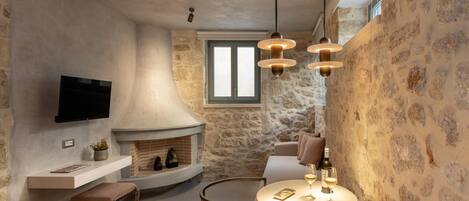 A cozy interior with a stone wall, a fireplace, a flat-screen TV, a round dining table with chairs, and pendant lighting.