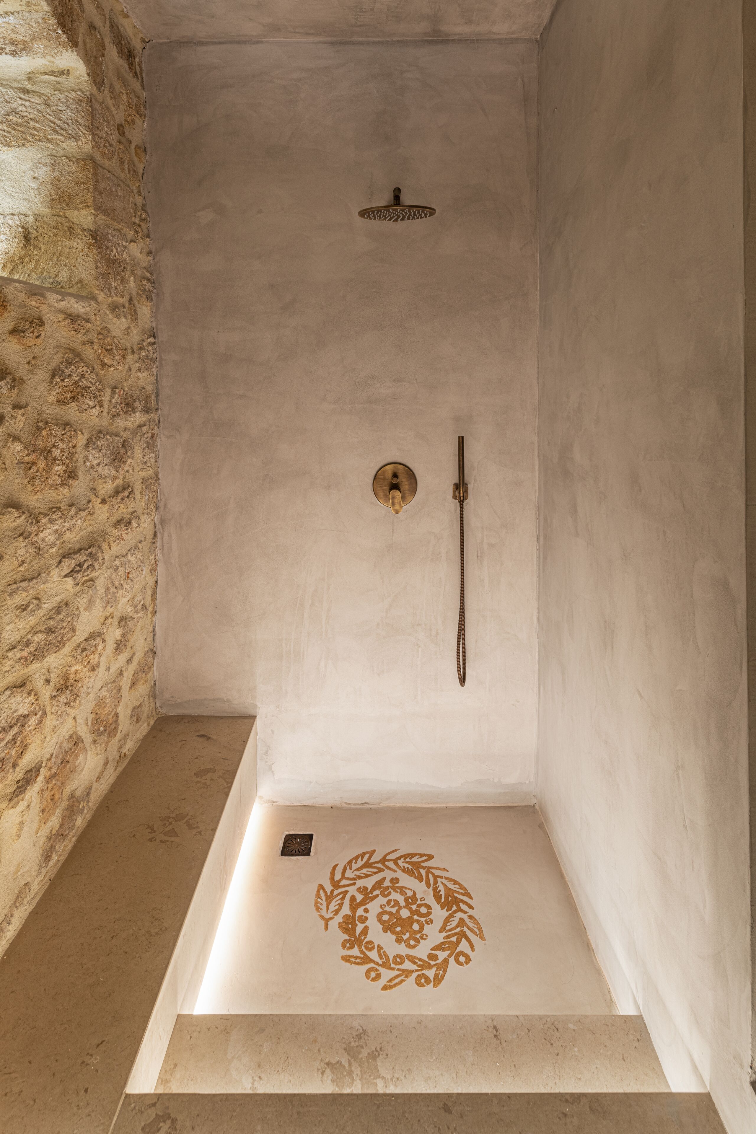 Ducha con pared de piedra a un lado, un cabezal de ducha y un cabezal de ducha de mano.