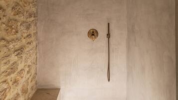 Ducha con pared de piedra a un lado, un cabezal de ducha y un cabezal de ducha de mano.