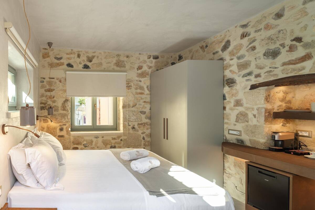 Une chambre avec un mur en pierre, un lit avec du linge de lit blanc, une armoire et un appareil à café intégré.