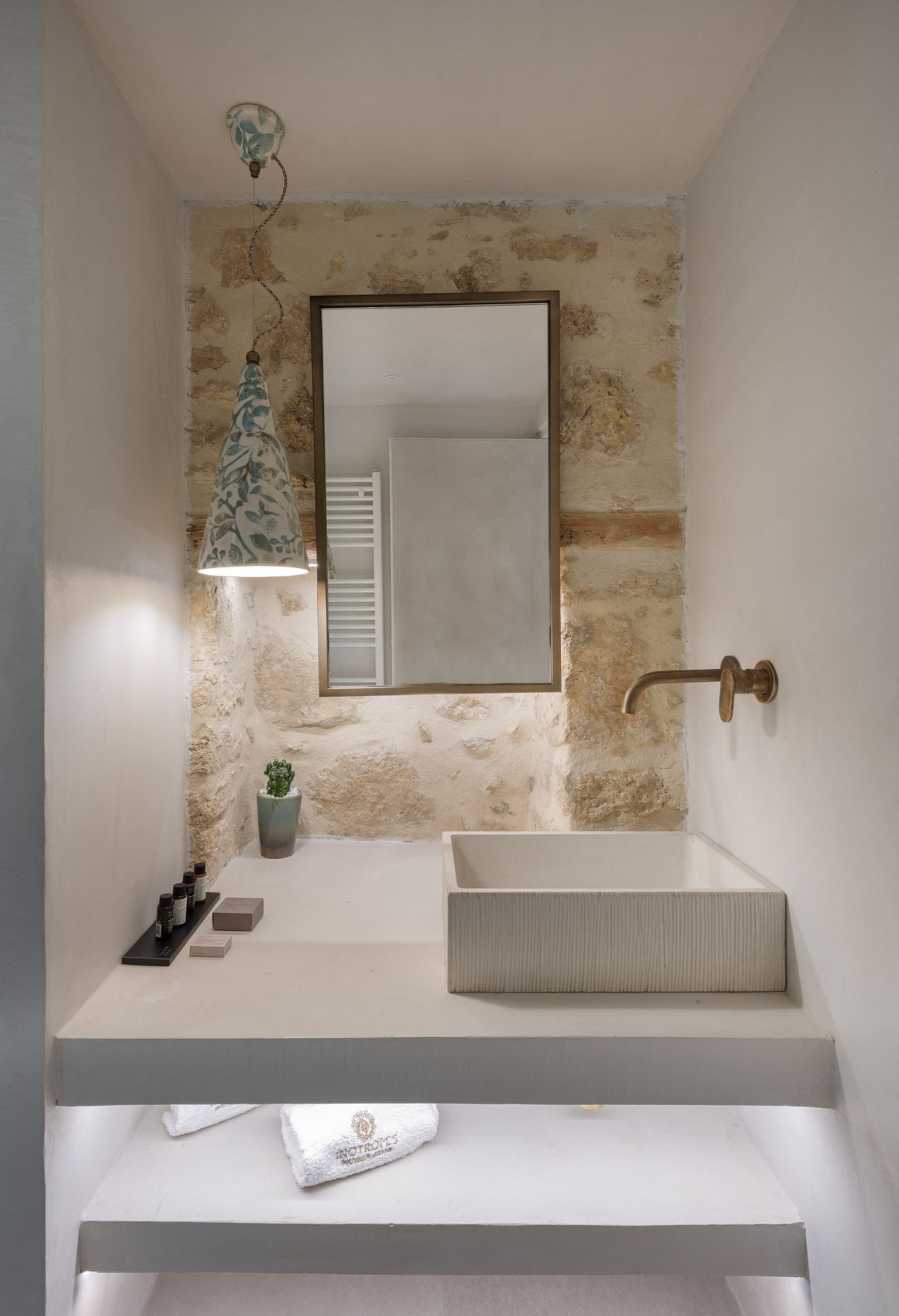 A bathroom with a white sink, a mirror, a hanging light fixture, and a small potted plant.