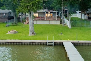 A lakeside cabin with a deck, a dock, and a grassy yard. - Lakefront lodging that your family will love (Mabank)