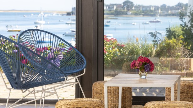En balkon med fletmøbler, en blomstervase og udsigt til både på vandet.