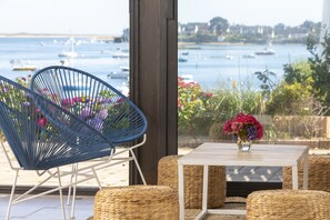 Un balcón con muebles de mimbre, un jarrón de flores y vista a barcos en el agua.