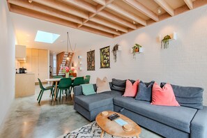 Una sala de estar moderna con un sofá seccional gris, una mesa de centro de madera y un comedor con sillas verdes.