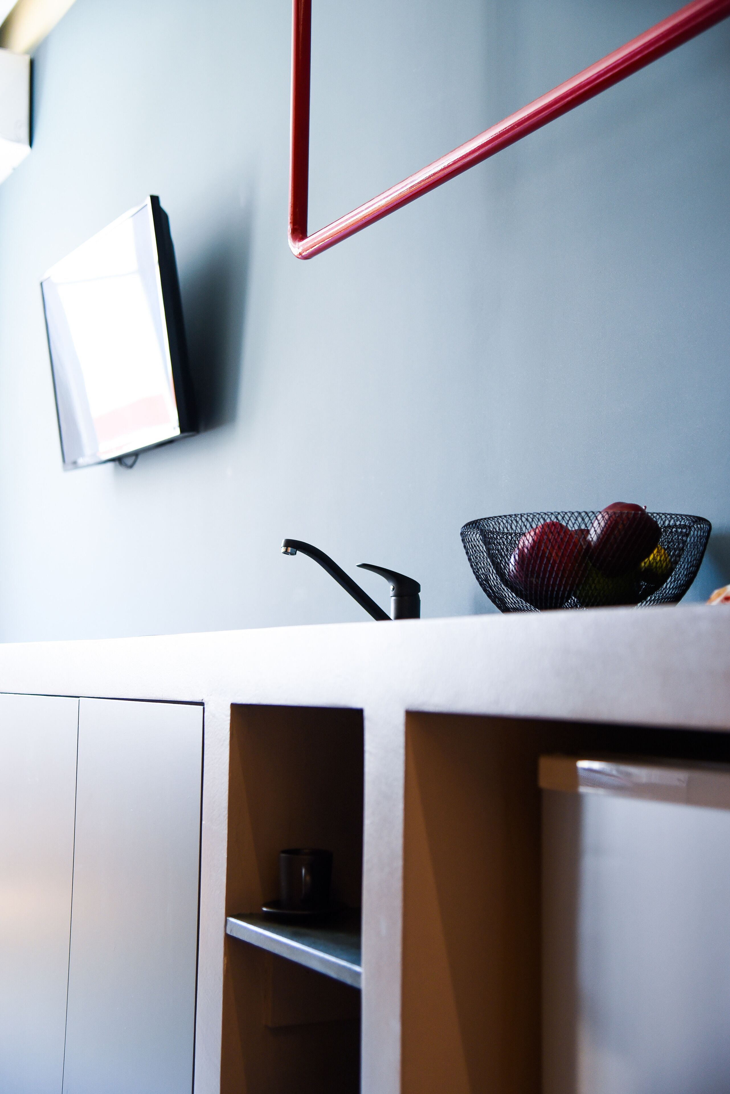 A modern kitchen with a white countertop, a red handle, a black sink, and a fruit basket.