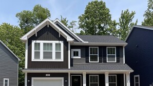 A two-story house with a garage, a front porch with red chairs, and a stone accent wall. - Harbor Hideaway - 3 bedroom cottage. (South Haven)