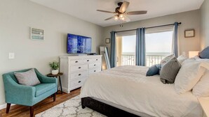 Un dormitorio con cama, ventilador de techo, cómoda, silla y vista a la playa.