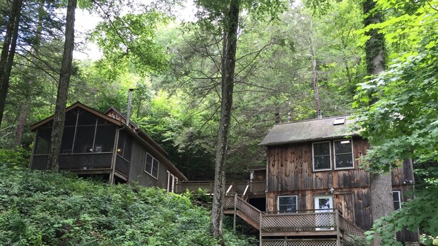A rustic cabin with a wooden exterior, surrounded by dense forest. It features a balcony and a staircase leading to an upper level. - Waterfront House and Artist's Studio in the Woods (Kent)