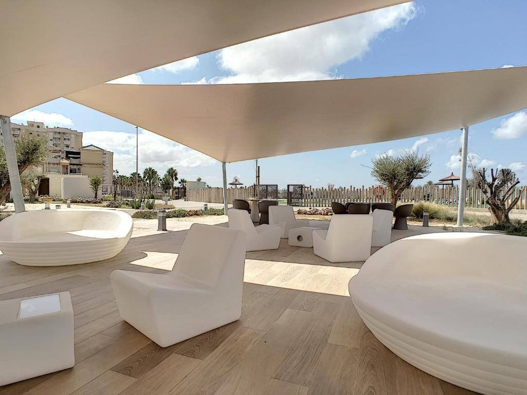 Un área de estar al aire libre con muebles blancos modernos y un paraguas grande que da sombra.