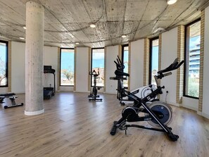 Un gimnasio espacioso con suelo de madera, ventanas amplias y diversos equipos de ejercicio.