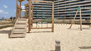 A beach with a wooden play structure and a large hotel building in the background. - Dreamy Sunset - Appartement (Playa Honda)