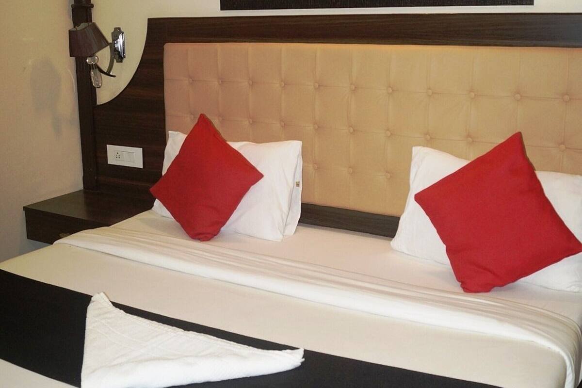 Ein Hotelzimmer mit einem Bett, zwei roten Kissen, einem gerahmten Bild an der Wand und einem Nachttisch mit einer Lampe.