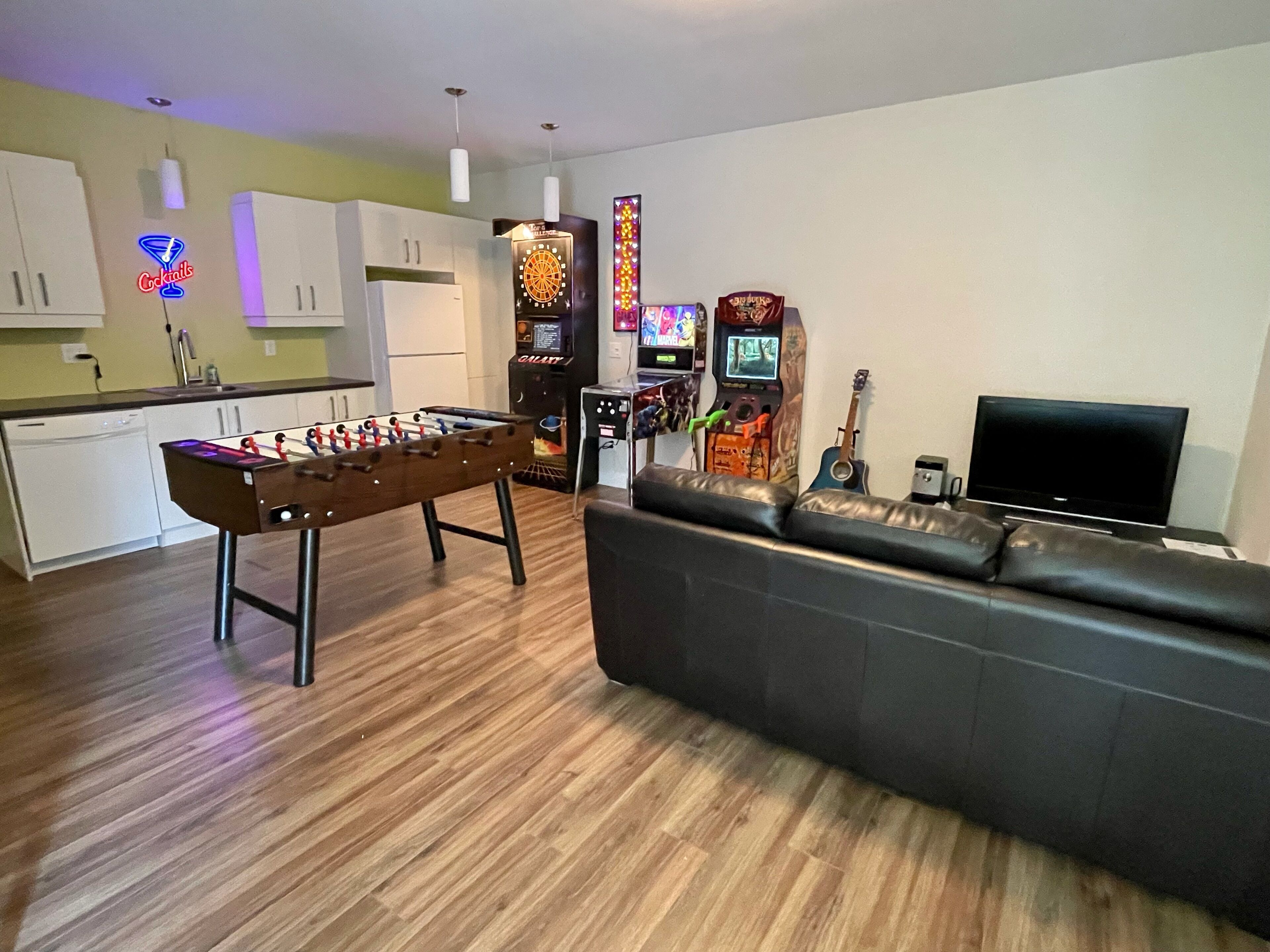 A living room with a foosball table, a sofa, a television, and arcade games.