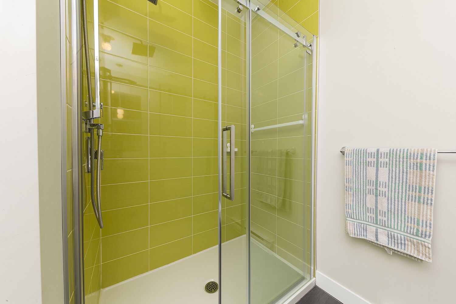 Eine begehbare Dusche mit Glaswänden, einer Handbrause, einer Glastür und einem Handtuchhalter mit gemustertem Handtuch.