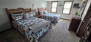 A bedroom with two beds, a nightstand, a dresser, a TV, and a window with blinds.