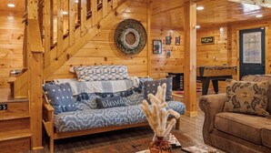 Acogedor interior de cabaña de madera con cama, sofá, mesa de centro y escalera.