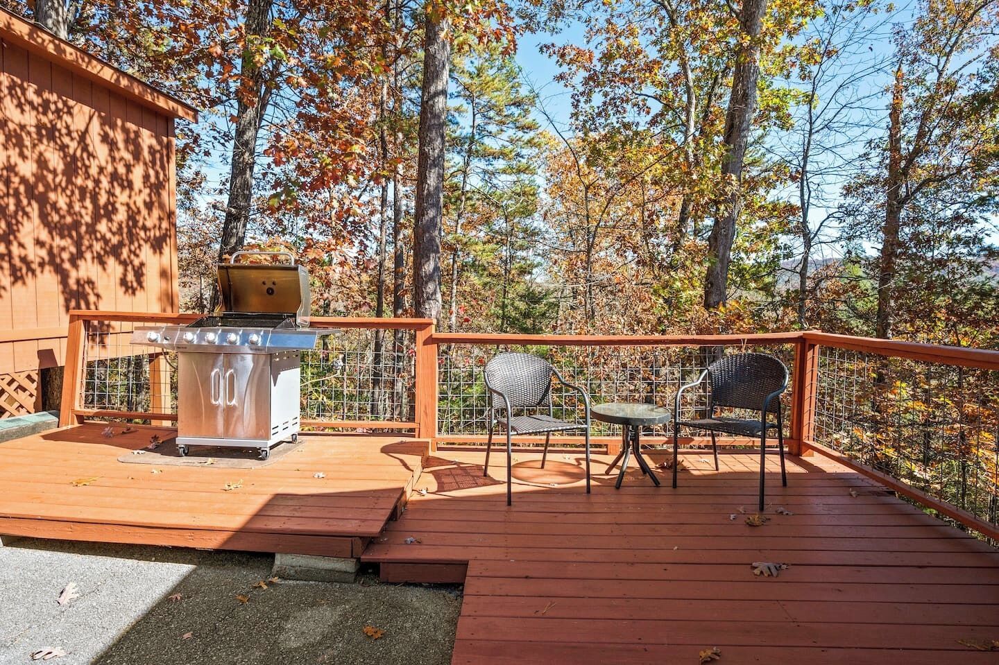 Una terraza de madera con una parrilla y dos sillas, rodeada de árboles.