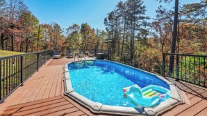 Una piscina con cubierta de madera, rodeada de árboles y barandilla de metal.