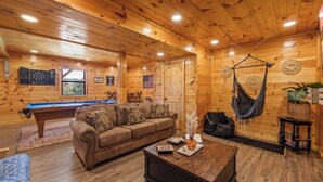 Un acogedor interior de cabaña de madera con mesa de billar, sofá, mesa de centro y hamaca.