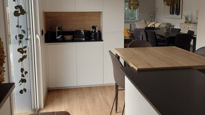 Eine moderne Küche mit weißen Schränken, einer Holzarbeitsplatte und einer schwarzen Theke. Im Vordergrund steht ein Holzstuhl und ein Esstisch mit Stühlen.