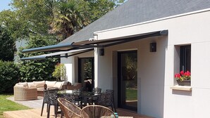 Eine Terrasse im Freien mit überdachter Sitzgruppe, einem Esstisch und Korbstühlen.