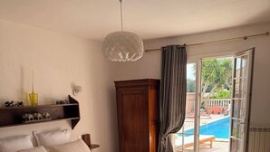 Un dormitorio con cama, armario de madera, lámpara colgante y vistas a una piscina exterior a través de una puerta corrediza de vidrio.