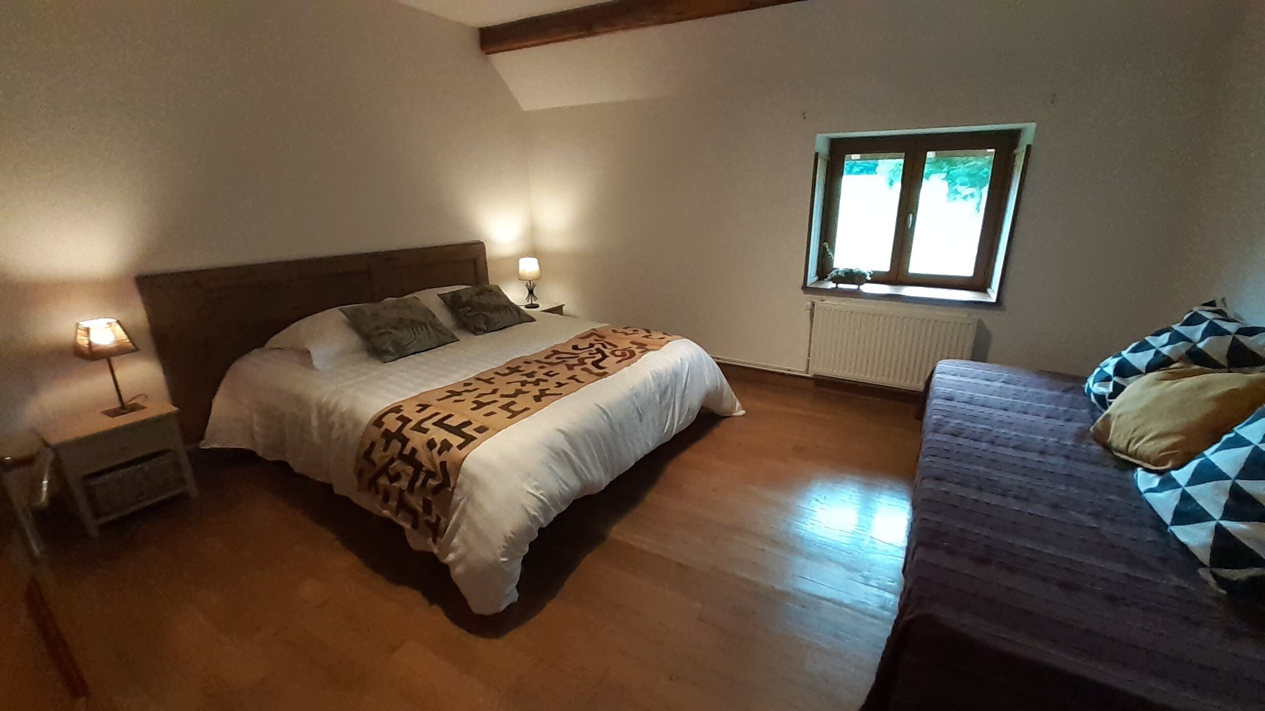 Un dormitorio con cama, mesita de noche, ventana y sofá.