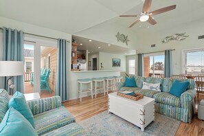 A spacious living room with a large sofa, a coffee table, and a dining area with bar stools. - Starry Nights: Oceanview, Private Pool, Hot Tub, Rec Room, Dog-friendly (Kill Devil Hills)