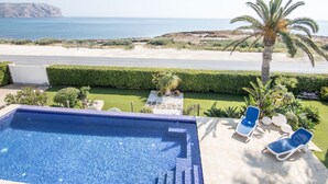 A pool with lounge chairs, a view of the beach, and a palm tree. - Villa Frente al mar con Vistas, Terraza, Barbacoa y Piscina con spa (Bahía de Jávea)