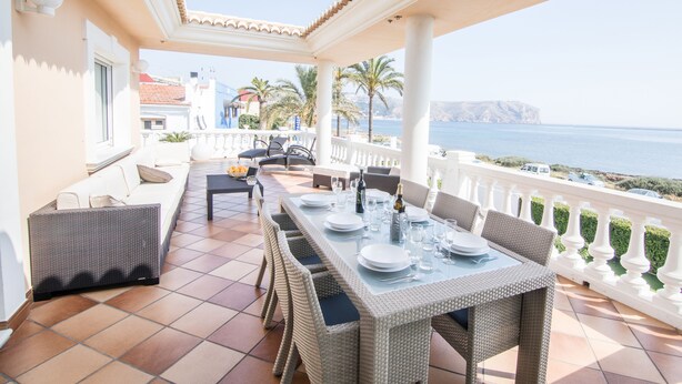A sunlit outdoor dining area with a terrace overlooking the sea, featuring wicker furniture and a tiled floor. - Villa Frente al mar con Vistas, Terraza, Barbacoa y Piscina con spa (Bahía de Jávea)