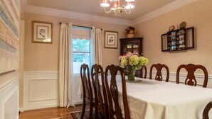 A dining room with a white table, wooden chairs, a vase of flowers, and a cabinet with decorative items. - High Street Hideaway (New Milford)