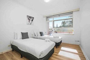 A bedroom with two beds, a large window, and a wall-mounted artwork.