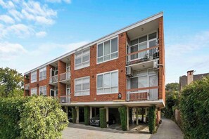 A multi-story residential building with a brick facade, multiple balconies, and a covered parking area. - Domi Rentals - The Meadow Gardens (Saint Kilda East)