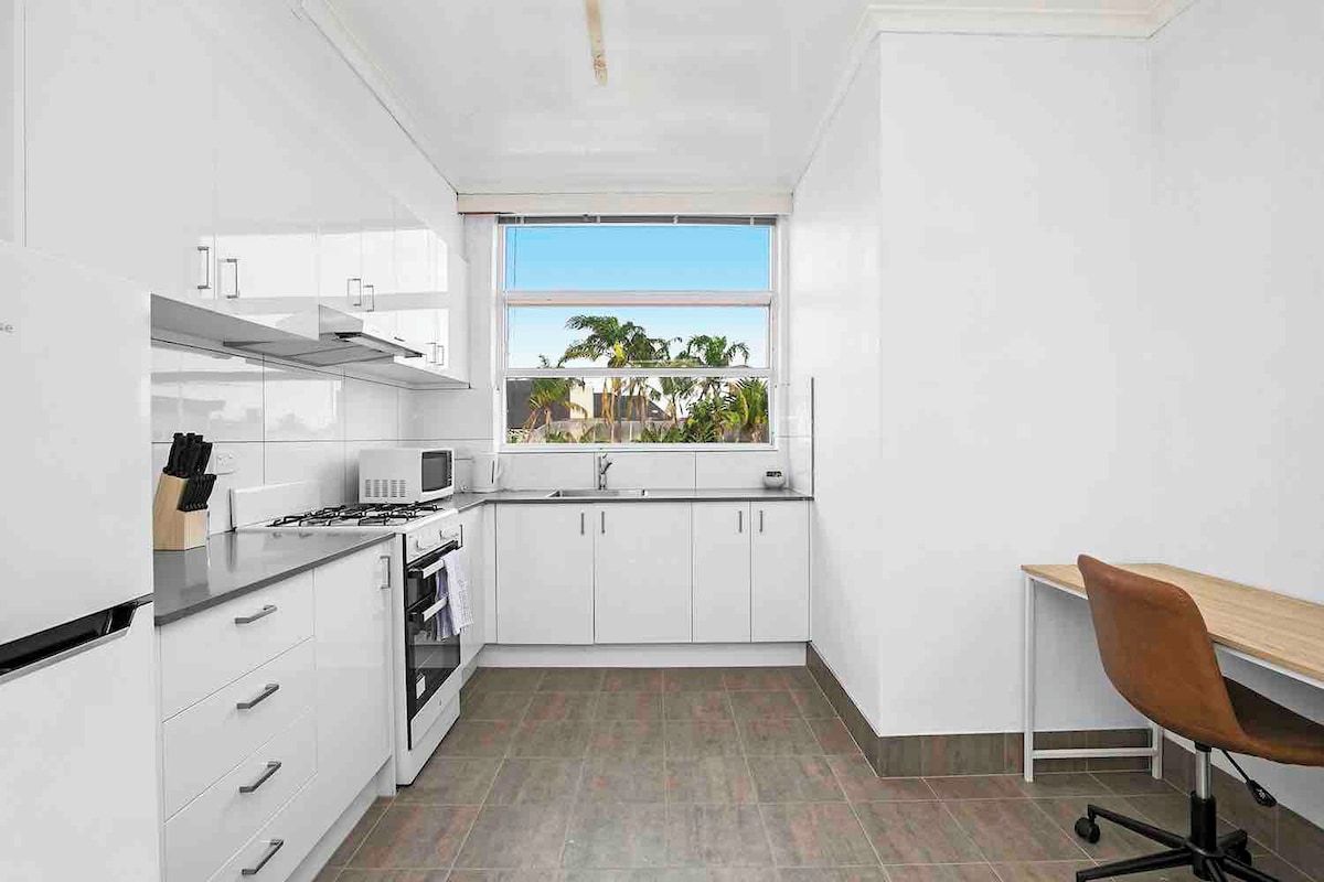 A modern kitchen with white cabinetry, a gas stove, and a window with a view of palm trees.