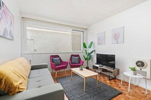 A modern living room with a sofa, two armchairs, a coffee table, a TV, and a plant.