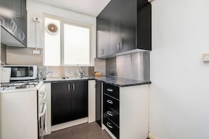 A compact kitchen with a microwave, stove, sink, and black cabinets.