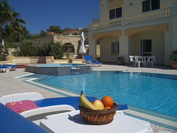 A swimming pool with lounge chairs and a fruit basket.