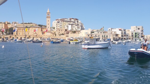 A marina with boats docked, a prominent tower, and buildings in the background. - Superb & comfortable 2-bedroom villa apt sleeps 5, swimming pool, AC/WiFi (Il-Mellieħa)