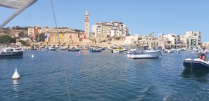 A marina with boats docked, a prominent tower, and buildings in the background.