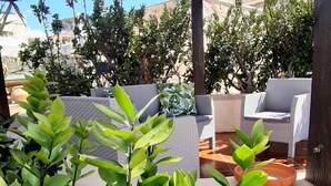 A covered outdoor seating area with lush green plants, wicker furniture, and a view of a desert landscape. - Superb & comfortable 2-bedroom villa apt sleeps 5, swimming pool, AC/WiFi (Il-Mellieħa)