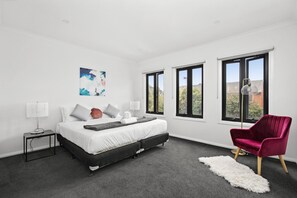 Relax in this serene bedroom with a large bed, plush pillows, and a stylish armchair.