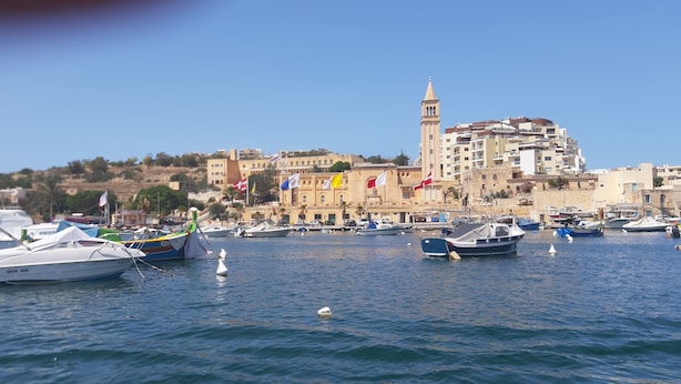 Marina com barcos atracados, um edifício imponente com torre e um céu azul límpido.