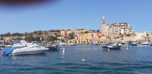 A marina with boats docked, a prominent building with a tower, and a clear blue sky. - Comfortable,1 bedroom apt sleep 2/3 persons with AC, swimming pool, & Wi-Fi. (Il-Mellieha)