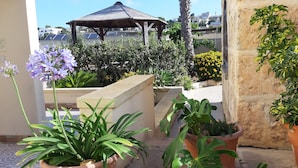 Um jardim no terraço com plantas em vasos, um gazebo e vista para edifícios ao fundo.