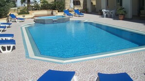Piscina com água azul, rodeada por espreguiçadeiras e plantas em vasos.