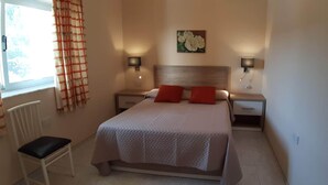Un dormitorio con una cama, dos mesitas de noche, una silla y una ventana con cortinas.
